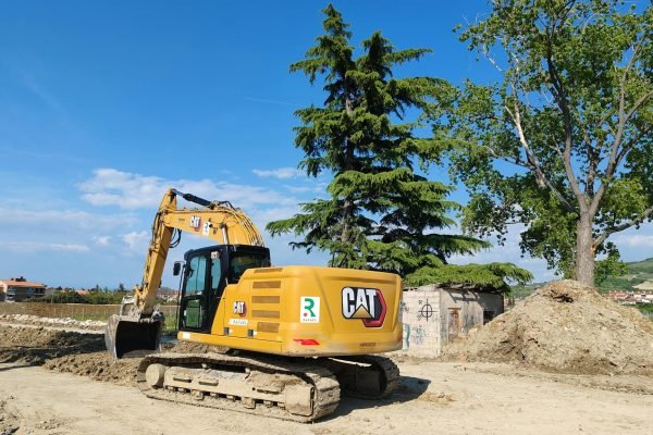 A CAT excavator working at a construction site with trees and blue sky in the background.