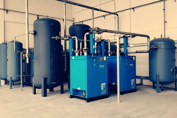 Industrial air compressor setup with blue tanks and pipes inside a plant.