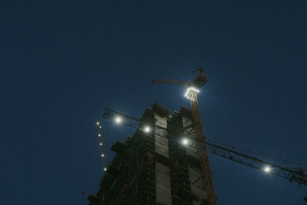 Illuminated tower cranes at a construction site captured during nighttime.